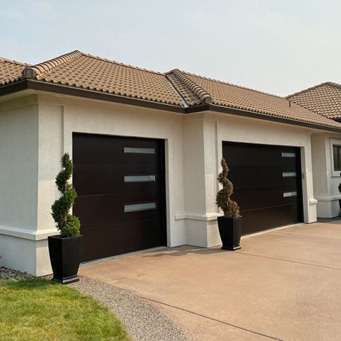 A garage featuring two doors, accompanied by a white fence, set against a clear sky backdrop