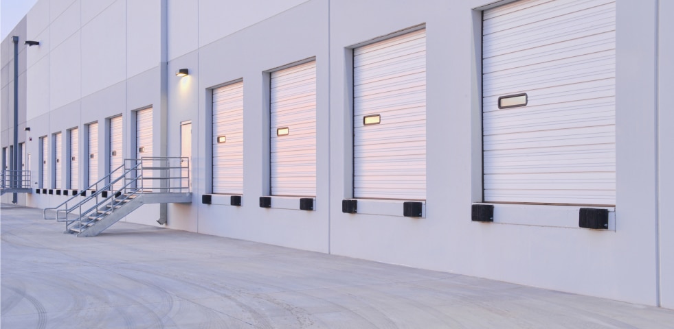 A large white building featuring multiple garage doors, set against a clear sky, showcasing its expansive structure