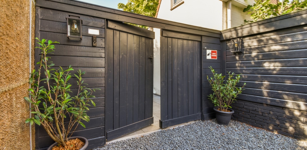 A black gate stands prominently, flanked by two decorative planters filled with vibrant plants