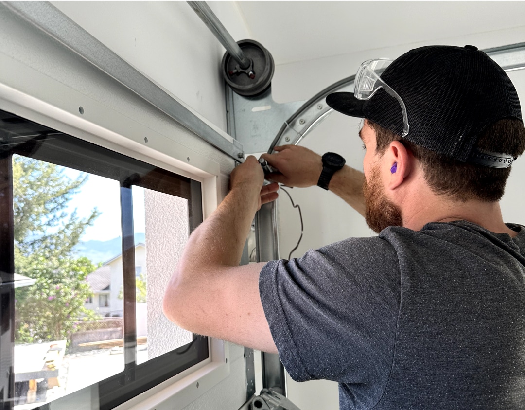 A man repairs a window in a garage, focused on his task with tools and materials surrounding him