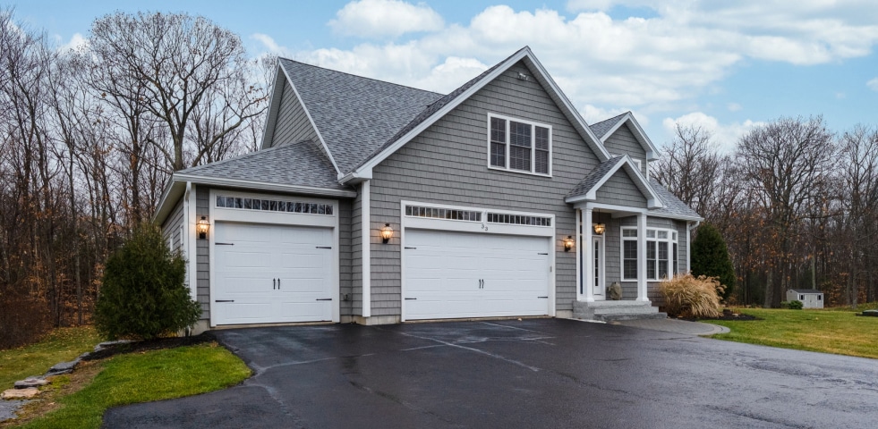 A gray house featuring a driveway and an attached garage, set against a clear sky backdrop