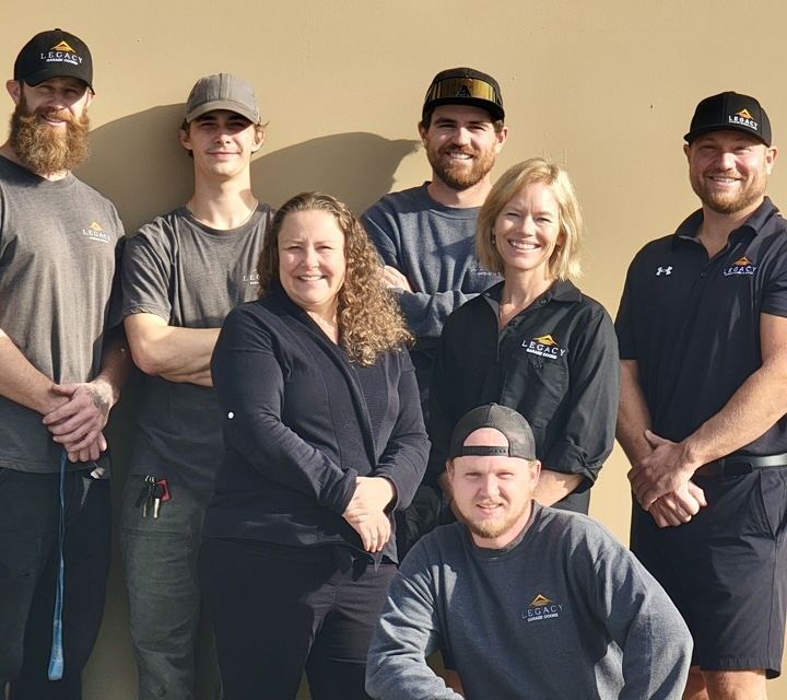 Legacy Garage Doors team in uniform smiling in front of a modern garage, representing Kelowna Garage Door Repair service