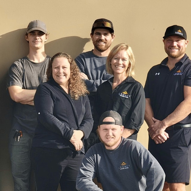 Legacy Garage Doors team in uniform smiling in front of a modern garage, representing Kelowna Garage Door Repair service